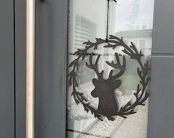 May include: A black metal reindeer head wreath with a black string hanging from a hook on a gray door.