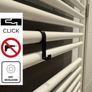 Puede incluir: Un gancho de plástico negro para colgar objetos en un toallero blanco. El gancho está diseñado para instalarse fácilmente sin necesidad de herramientas. El texto "CLICK" y "EASY INSTALLATION" es visible en la imagen.