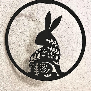 Könnte beinhalten: Schwarze Metallsilhouette eines Kaninchens mit floralen Details, die an einem runden Metallrahmen hängt.