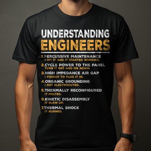 May include: Black t-shirt with the text "UNDERSTANDING ENGINEERS" in white and yellow. The shirt lists humorous definitions of engineering terms, including "Percussive Maintenance" and "Kinetic Disassembly."