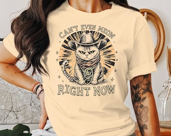 Könnte beinhalten: Ein hellgelbes T-Shirt mit einem Aufdruck eines Katers mit Cowboyhut und Bandana. Der Text "Can't Even Meow Right Now" ist auf dem Shirt gedruckt.
