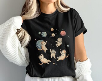 May include: Black t-shirt featuring a whimsical illustration of cats in space suits floating among planets and stars. The design includes various planets in shades of blue, orange, and brown, with the cats in a playful pose.