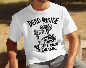 以下が含まれることがあります： サングラスをかけた白黒の骸骨が缶から飲んでいる白いTシャツ。テキスト「DEAD INSIDE BUT STILL DOWN TO DRINK」が骸骨のイラストの上と下に印刷されています。