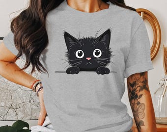 May include: A gray t-shirt with a black cat peeking over the top. The cat has big, round eyes and a pink nose.