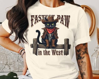 Pode incluir: Camiseta creme com um gato preto vestido de cowboy, completo com chapéu, colete e botas. O gato está segurando uma arma e sentado em uma cerca de madeira. O texto acima e abaixo diz "Fastest Paw in the West."
