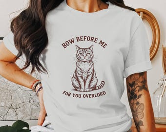 Może przedstawiać: Biała koszulka z brązową ilustracją siedzącego kota z nadrukiem "Bow Before Me For You Overlord".