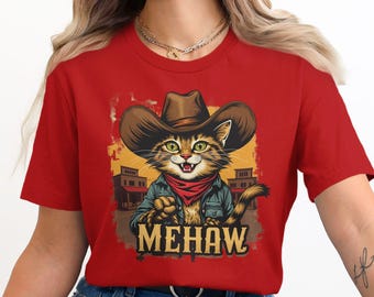Könnte beinhalten: Rotes T-Shirt mit einer Cartoon-Illustration einer Katze, die einen Cowboyhut und ein Bandana trägt. Die Katze hält eine Pistole und der Text "MEHAW" ist unter der Katze aufgedruckt.