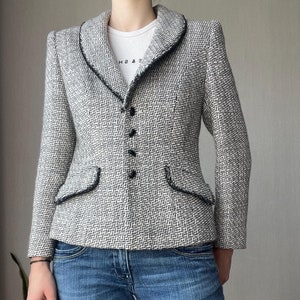 Peut inclure: Un blazer en tweed noir et blanc avec une bordure noire autour du col et des poches. Le blazer a une fermeture à boutons et une silhouette ajustée.