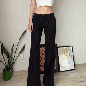 Puede incluir: Pantalón negro de rayas finas con pierna ancha. El pantalón tiene cierre de botón y cremallera y está hecho de una tela ligera.