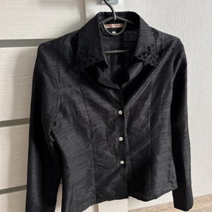 May include: A black long-sleeved button-up shirt with a lace collar. The shirt has a textured fabric and a small label that reads "Daniel & Mayer" on the collar.