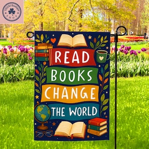 May include: A navy blue garden flag with the words "READ BOOKS CHANGE THE WORLD" in white, yellow, and green. The flag features illustrations of books, a globe, a coffee cup, and glasses. The flag is displayed in a garden.
