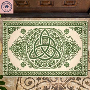 Könnte beinhalten: Rechteckige Fußmatte mit cremefarbenem Hintergrund und einem grünen keltischen Knotendesign. Das Design umfasst einen zentralen Triquetra-Knoten, Kleeblätter und dekorative Bordüren. Die Matte liegt auf einem gemusterten Fliesenboden.