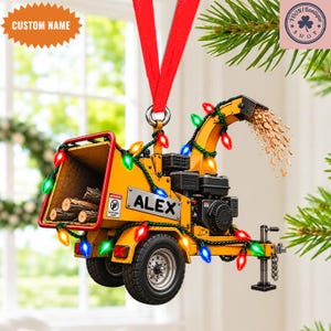 Op de afbeelding: Een gele houtversnipperaar-ornament hangend aan een rood lint, versierd met veelkleurige kerstverlichting. De machine heeft de naam ALEX op de zijkant, een trechter gevuld met houtblokken en houtsnippers die uit de uitwerpschacht komen.