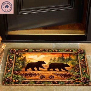 Puede incluir: Felpudo rectangular con una escena de bosque con dos osos pardos caminando. La alfombra tiene un borde de cuerda con piñas y vegetación. El fondo muestra una puesta de sol y árboles. Se ven huellas de patas.