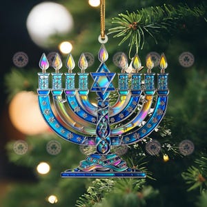 May include: A Hanukkah menorah ornament with a stained glass appearance. The blue and iridescent menorah features nine candle holders with flames, a Star of David, and decorative details. It hangs from a gold cord against a blurred background of a Christmas tree.