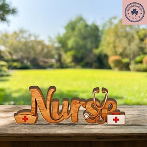 May include: Wooden decorative sign spelling "Nurse" with a stethoscope, nurse's hat, and medical kit. The sign is made of light brown wood and has a red cross on the hat and kit. The background is a blurred outdoor scene.