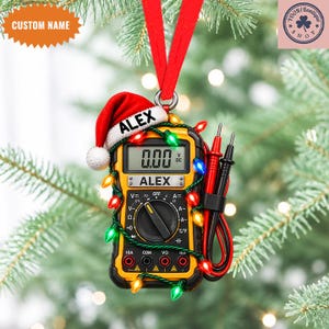 May include: A yellow and black digital multimeter Christmas ornament featuring a red Santa hat with the name ALEX printed on the brim and the device face. The multimeter is wrapped in a string of colorful Christmas lights and includes test leads.
