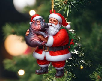 May include: A Christmas ornament featuring Santa Claus in a red suit and hat, holding a baby hippo. Both figures wear matching Santa hats. The ornament is a 2D flat item, hanging against a backdrop of a Christmas tree.