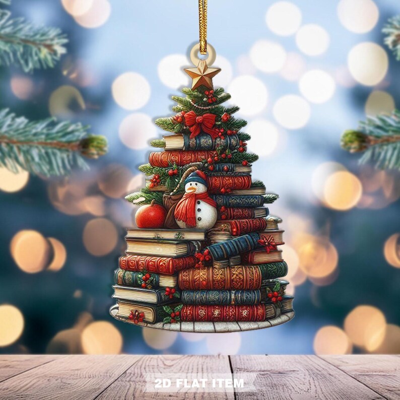 May include: A Christmas tree ornament shaped like a tree made of books. The ornament features a snowman, red bow, and star. The text "2D FLAT ITEM" is at the bottom. The ornament hangs from a gold string.