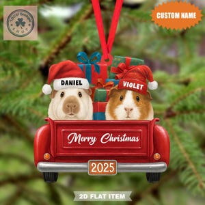 Könnte beinhalten: Weihnachtsschmuck mit zwei Meerschweinchen mit Weihnachtsmützen, namens Daniel und Violet, in einer roten Ladefläche voller Geschenke. Der Schmuck trägt die Aufschrift "Merry Christmas" und "2025". Ein rotes Band ist zum Aufhängen befestigt.