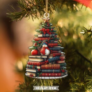 May include: Christmas tree ornament shaped like a stack of books, with a snowman, red bow, and star. The ornament is decorated with red berries and a small apple. The text "2D FLAT ITEM" is at the bottom.