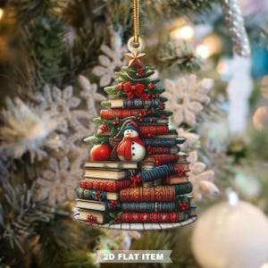 May include: A Christmas tree ornament shaped like a stack of books, with a snowman and red apple. The ornament is topped with a star and a bow. The text "2D FLAT ITEM" is at the bottom.