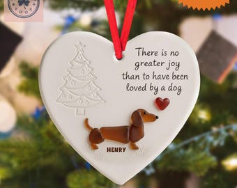 May include: Heart-shaped white ceramic ornament with a red ribbon. Features a dachshund dog, a Christmas tree, and the text "There is no greater joy than to have been loved by a dog." Includes the name "HENRY".