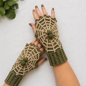 May include: A pair of fingerless crochet gloves in olive green and beige. The gloves feature a beige spiderweb pattern across the back of the hand, accented with a small, three-dimensional olive green spider. The cuffs are ribbed olive green.