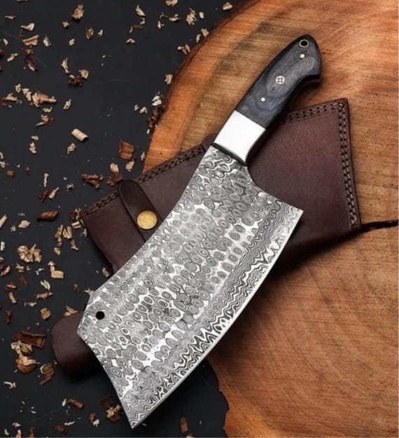 A single, hefty hand-forged Damascus cleaver with that hypnotic layered-steel pattern — the kind of blade that becomes the centerpiece of a kitchen.