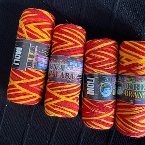 May include: Four spools of red and yellow yarn with labels. The yarn is wound in a zig-zag pattern. The labels have text in English and other languages. The yarn is likely used for crafting or religious purposes.
