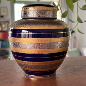 Op de afbeelding: Een blauwe en gouden keramische pot met een deksel. De pot heeft een decoratief patroon van gouden en zilveren lijnen en bloemmotieven.