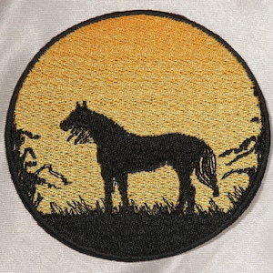 Può includere: Toppa rotonda ricamata raffigurante la silhouette di un cavallo nero contro un tramonto dorato. Il cavallo è in un campo erboso, con alberi e fogliame. La toppa ha un bordo nero.
