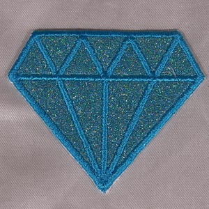 May include: A turquoise diamond-shaped patch with a glittery interior and a stitched outline. The patch is set against a light grey fabric background. The design features internal lines that create facets.