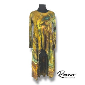 May include: A long-sleeved, high-low tunic top with a colorful abstract print in shades of brown, yellow, green, and blue. The top has a round neckline and long sleeves. The fabric is soft and flowy.
