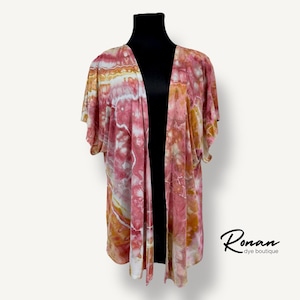 May include: A pink and orange tie-dye kimono with short sleeves. The kimono is open in the front and has a V-neck. The fabric has a marbled pattern.