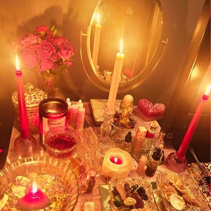 May include: A mystical altar setup with lit candles, a mirror, and various spiritual items. The scene includes red roses, glass bowls, and small bottles, creating a warm, inviting ambiance. The candles are of varying sizes and colors, adding to the spiritual theme.