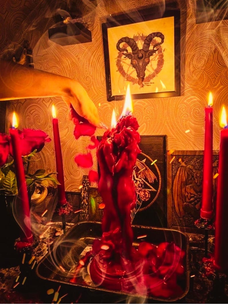 May include: A ritual scene featuring a large red candle shaped like two figures embracing, surrounded by burning red candles and rose petals. A framed image of a goat's head is visible in the background, along with other occult symbols.