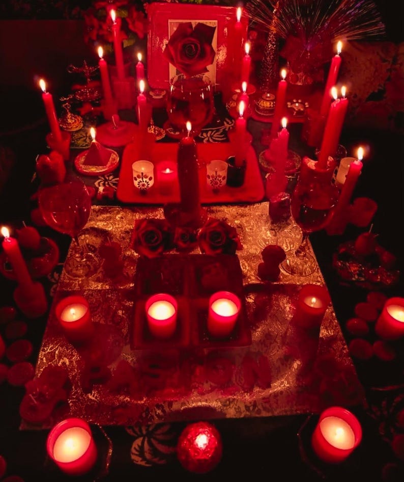 May include: A collection of red candles of various sizes and shapes, some lit, arranged on a table. The arrangement includes roses, small candle holders, and decorative items, creating a warm, inviting ambiance. The overall theme suggests a spiritual or decorative setting.