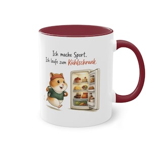 Könnte beinhalten: Ein weißer Keramikbecher mit dunkelrotem Innenraum und Henkel. Auf der Vorderseite ist ein Cartoon-Hamster mit Stirnband und grünem Shirt abgebildet, der zu einem offenen, mit Lebensmitteln gefüllten Kühlschrank läuft, inklusive dem Text Ich mache Sport. Ich laufe zum Kühlschrank.