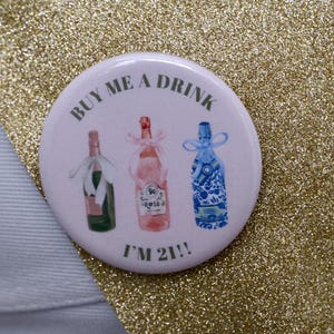 May include: A white button with the text "Buy me a drink I'm 21!" and three illustrated bottles of wine. The bottles are a green champagne bottle, a pink rose wine bottle, and a blue and white patterned bottle.
