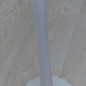 May include: A white vertical stand featuring a tall, slender cylindrical post attached to a circular base with a scalloped, wavy edge. The entire structure is uniform in color and has a smooth, matte finish, designed to hold items upright.
