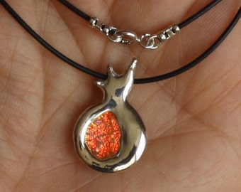 Peut inclure: Un collier en argent avec un pendentif en forme de grenade. Le pendentif est rempli de paillettes orange.