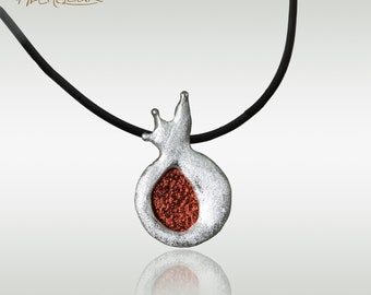 Peut inclure: Un collier en argent avec un pendentif en forme de grenade. Le pendentif est ouvert et montre un intérieur rouge texturé.