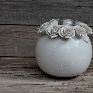 May include: White ceramic vase with a round shape and a ring of white ceramic roses around the top.