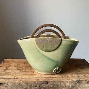 Könnte beinhalten: Eine grüne Keramikschale mit einem braunen, runden Räucherstäbchenhalter. Die Schale hat eine hellgrüne Glasur mit einem dunkleren grünen Wirbel.