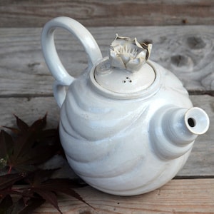 May include: White ceramic teapot with a textured, wavy design. The teapot has a flower-shaped lid and a spout.