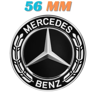 May include: A black and silver Mercedes-Benz emblem with a three-pointed star in the center. The emblem is surrounded by a silver ring with the words "MERCEDES" and "BENZ". The text "56 MM" is displayed above the emblem.