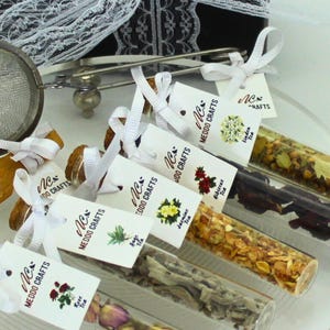 May include: Assortment of six small glass vials filled with loose leaf tea blends. Each vial is tied with a white ribbon and a small white tag with the text "Nex Meddo Crafts" and the name of the tea blend. The tea blends include Hibiscus Tea, Jasmine Tea, Linden Tea, Rose Tea, and two other blends.