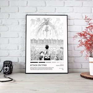 May include: A framed black and white print of the anime series "Attack on Titan" is displayed against a white brick wall. The artwork shows a dramatic scene with figures and buildings. A vintage camera is positioned in front of the print.