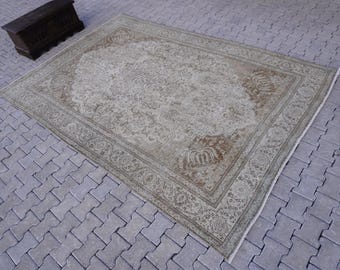 May include: A vintage rug with a light beige background and a floral pattern in shades of brown and green. The rug has a faded look and a worn texture.